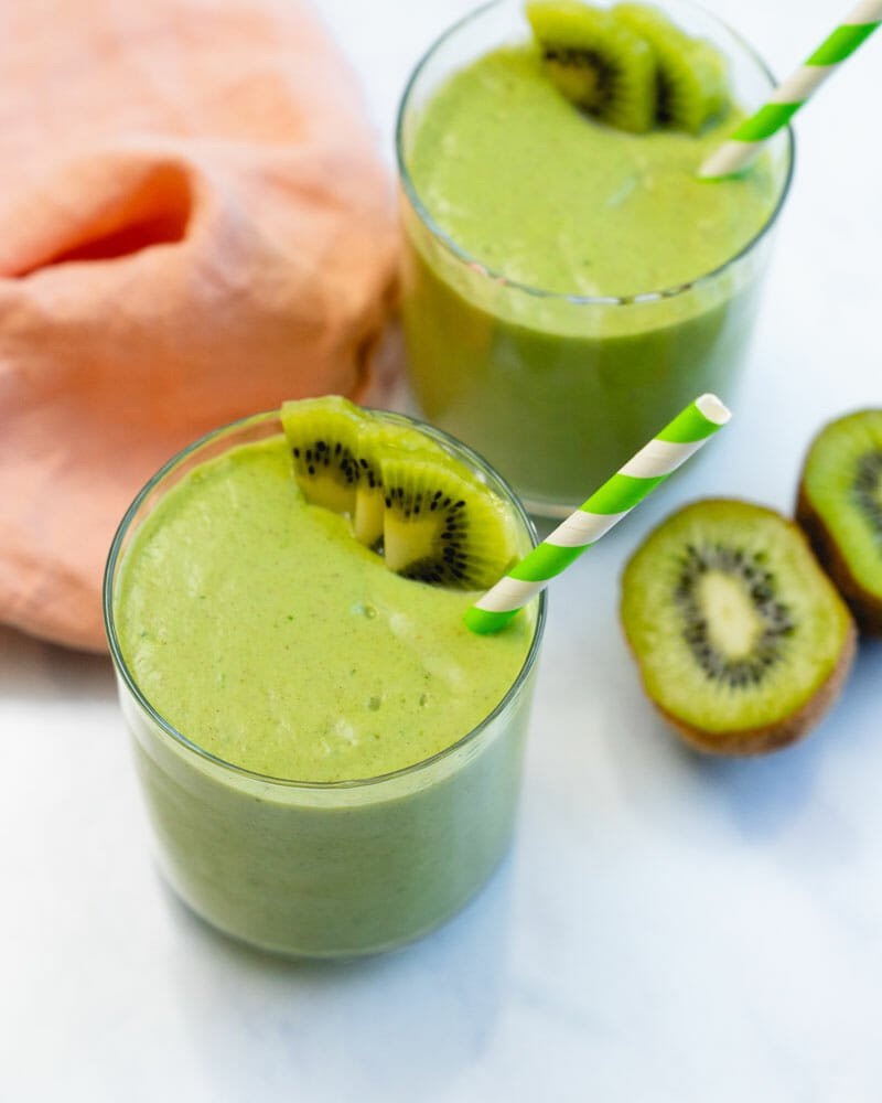 Green smoothie in glass with green and white striped straw and slices of kiwi.