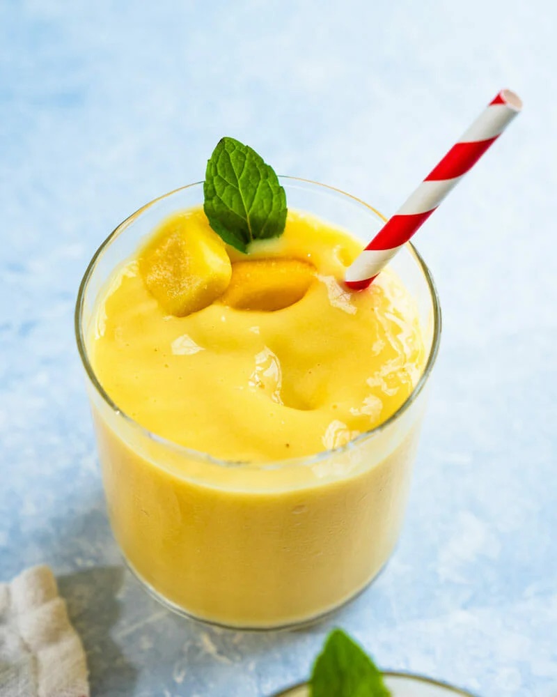 Bright yellow smoothie in a glass with red and white straw.