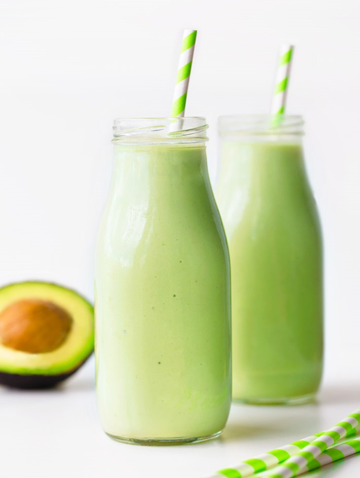 Two milk bottles full of pale green smoothie, both have a green and white straw. 