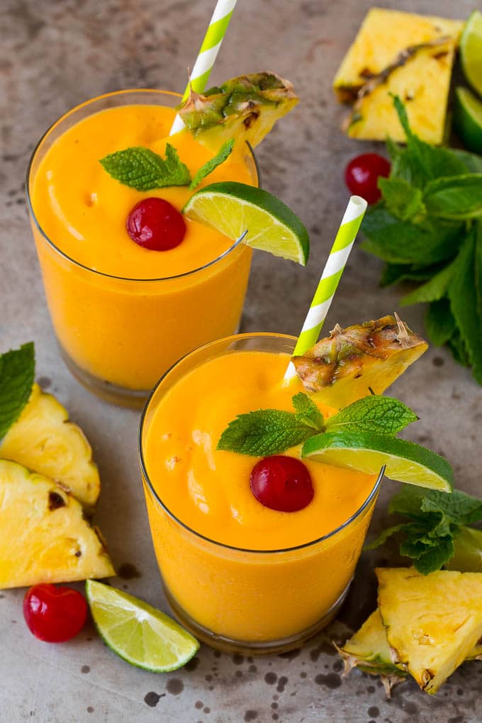 Bright orange smoothie in a glass with a cherry, sliced lime, mint leaf, and sliced pineapple on the glass,