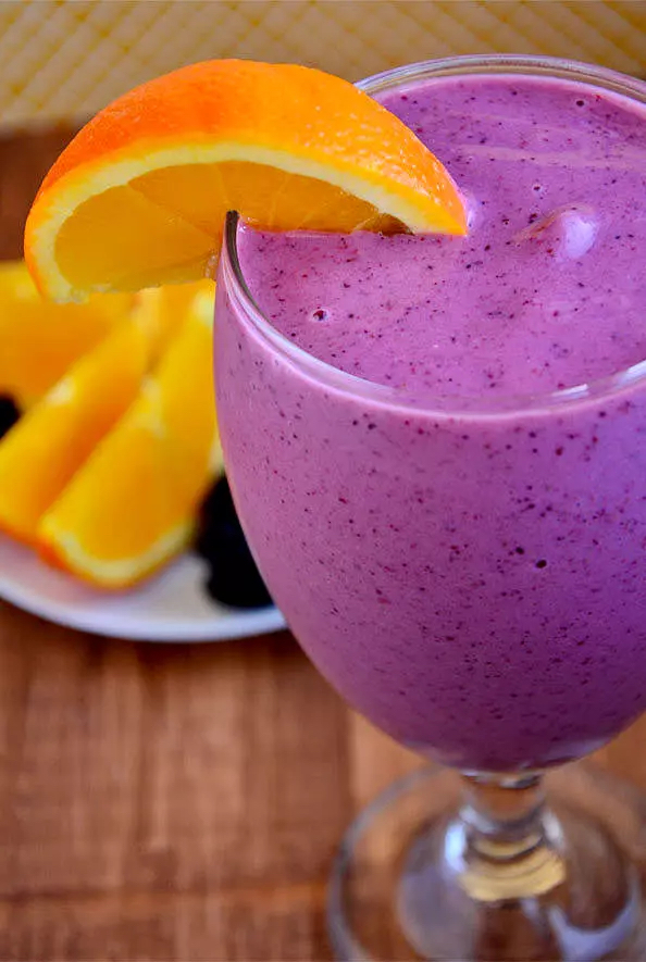 Bright purple smoothie in a glass with slice of orange on edge of glass.