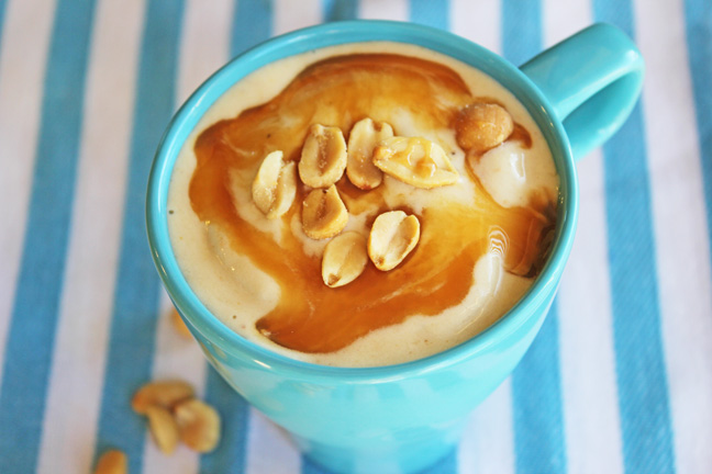 Smoothie in a blue mug with peanuts on top, on a blue striped tablecloth.