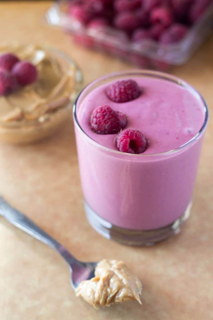 Bright pink smoothie in glass with raspberries on top.