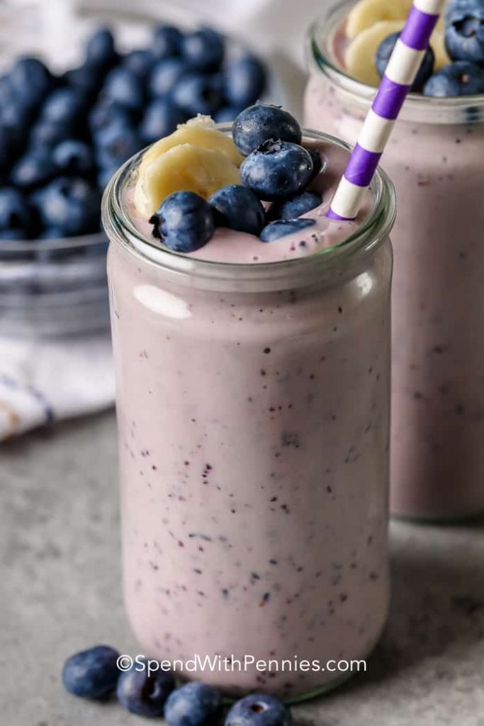 Pale purple smoothie in jar with striped straw and blueberries and banana slices on top.