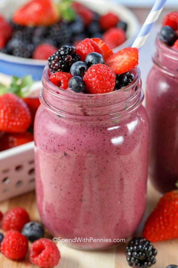 Dark red berry smoothie in a jar, with fresh fruit on top.