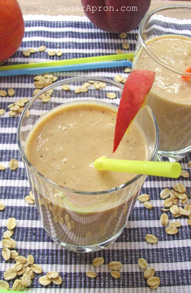 Glass of pale brown smoothie with green straw and slice of fruit.
