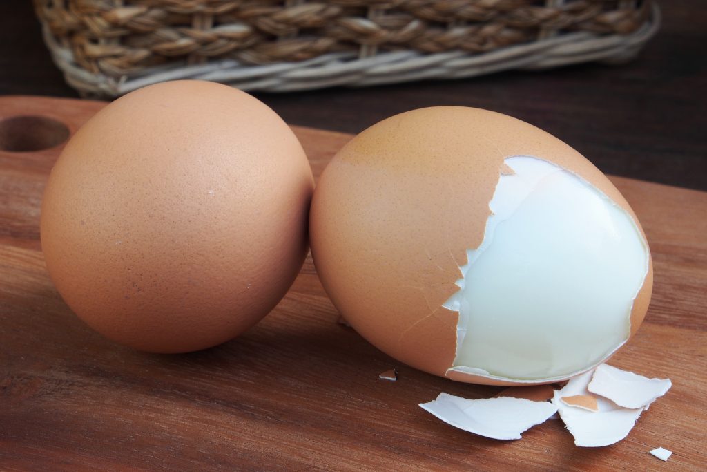 Two hard boiled eggs on a wooden board, one with shell partly peeled off.