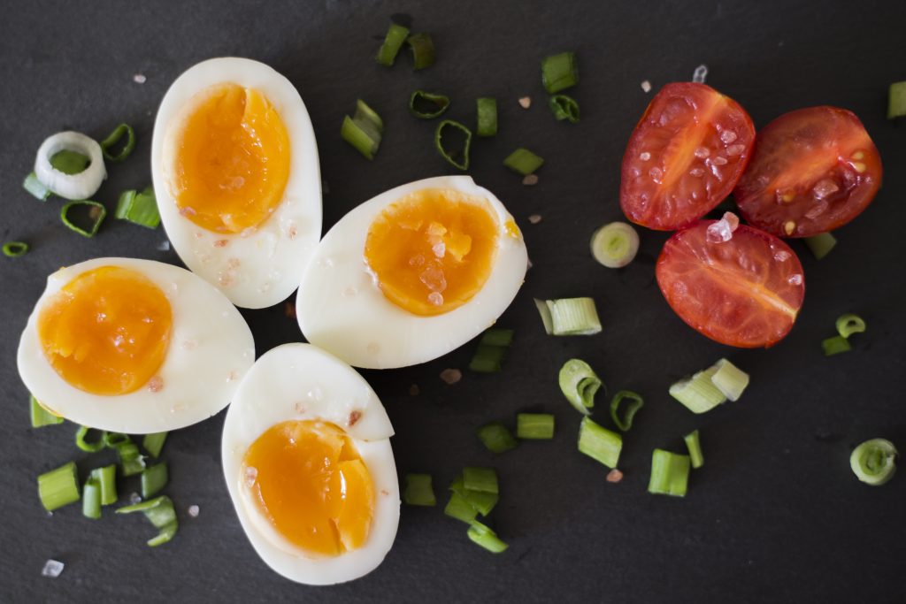 Four halved soft boiled eggs on a dark gray background with sliced tomatoes and spring onions.