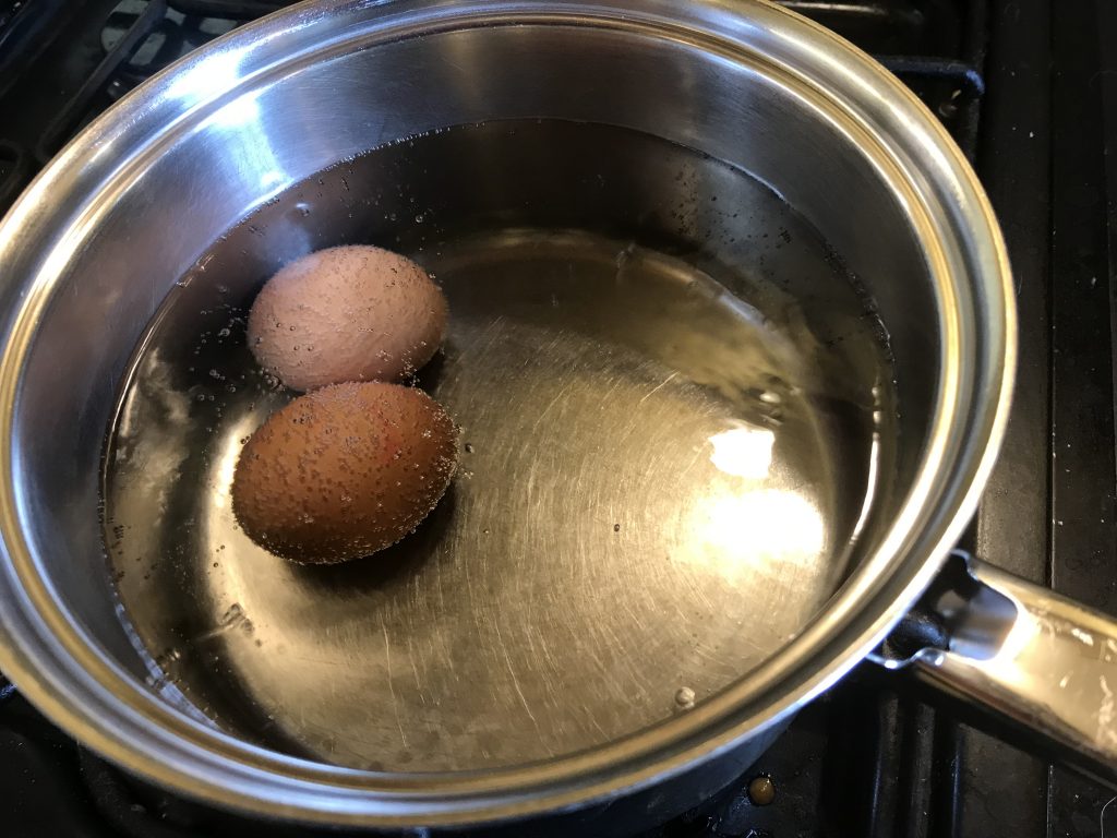 Two eggs covered with water and bubbles in a pan.