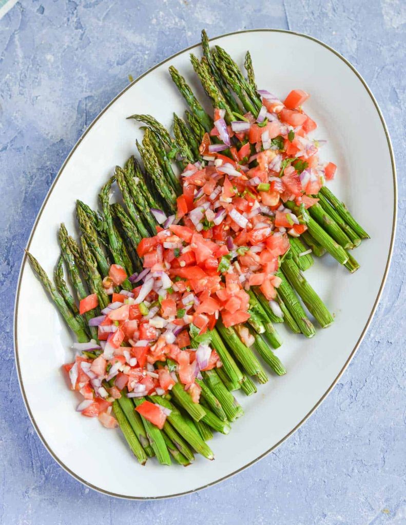 Roasted asparagus laid on white oval plate with tomato and onion garnish on top