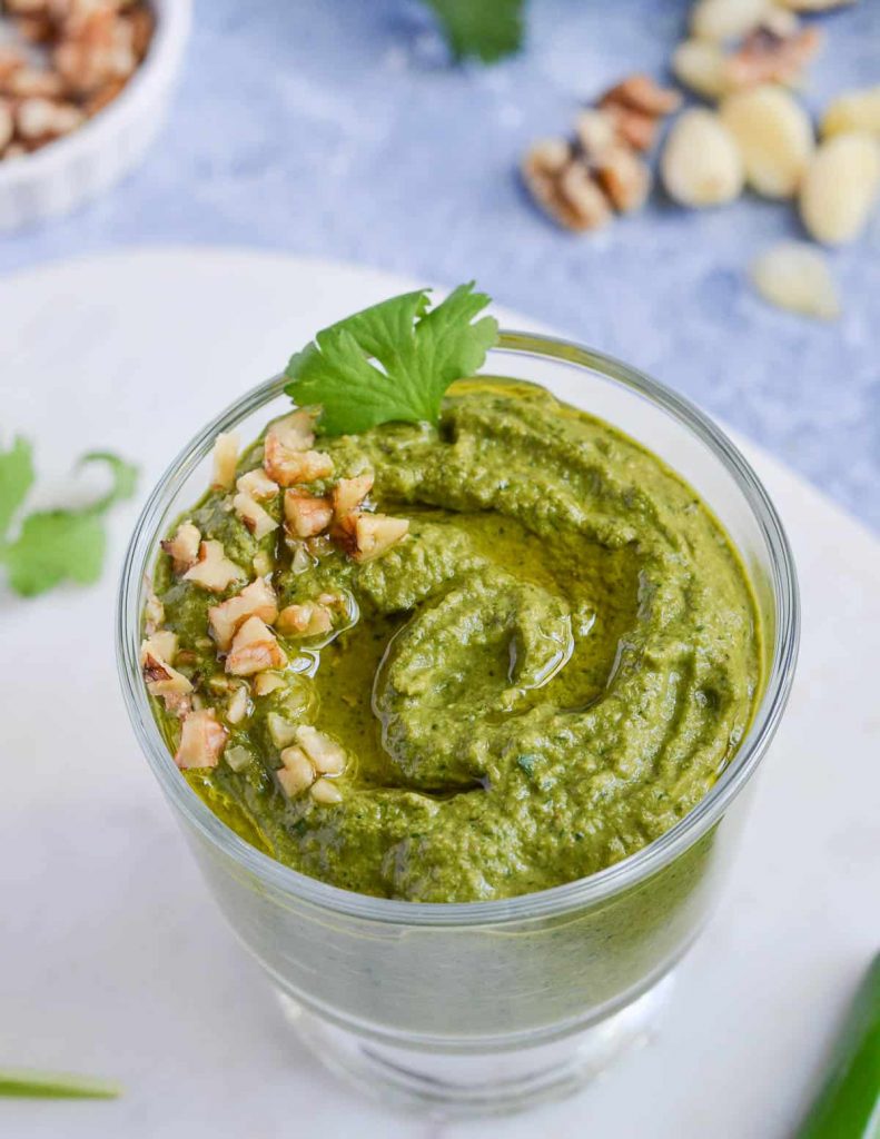 Glass containing green pesto with chopped nut garnish