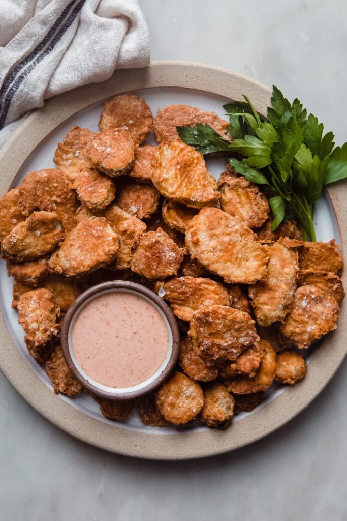 Air fried battered pickles with dip and herb garnish