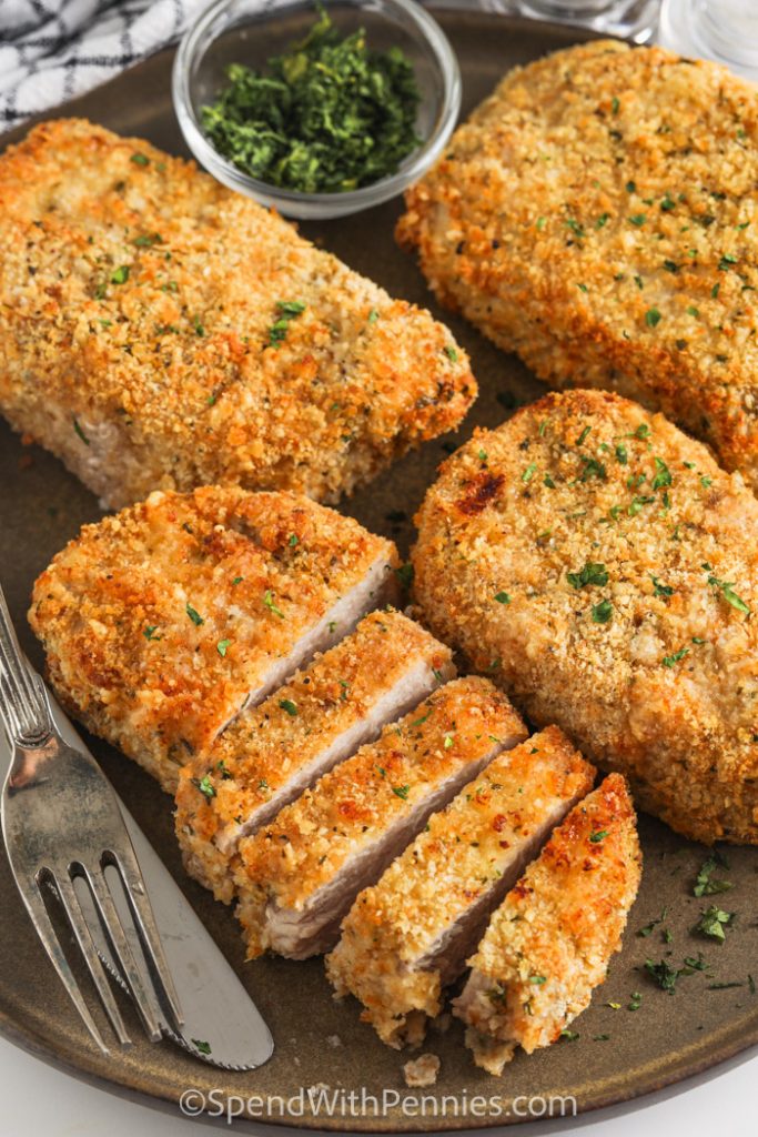 Breaded Pork chops, one sliced, on brown tray with knife and fork