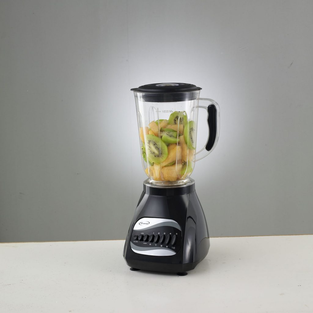 A black blender on a gray surface. The jar is filled with kiwi fruit and pineapple ready to blend.