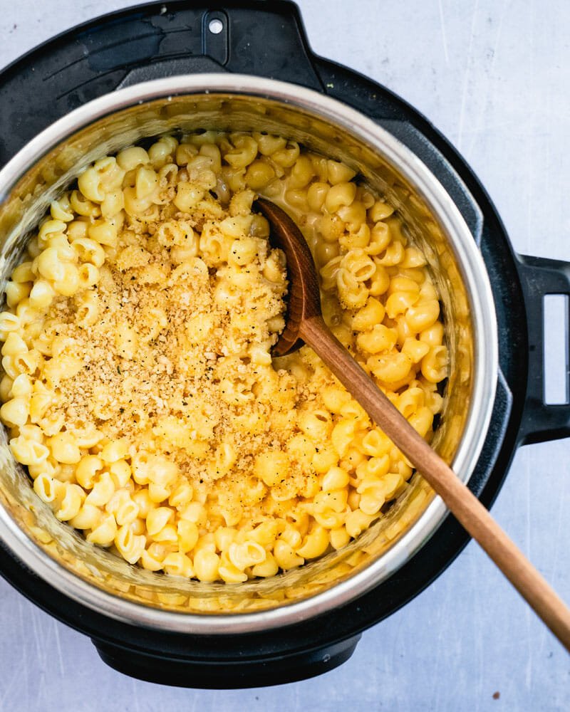 Macaroni cheese in silver and black cooking pot being scooped with wooden spoon