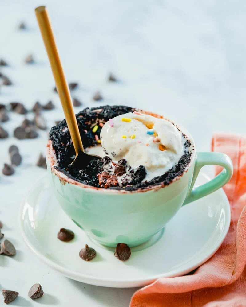 Sticky chocolate mug cake with cream on top and spoon sticking out