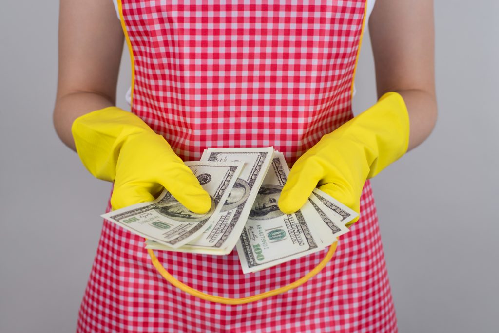 Woman in red and white checked apron with yellow rubber gloves holding lots of 100 dollar bills