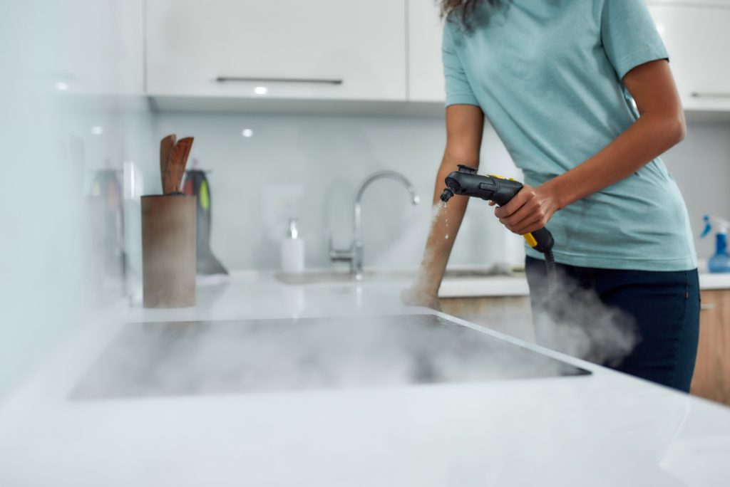 Woman cleaning kitchen with a steam-cleaner.