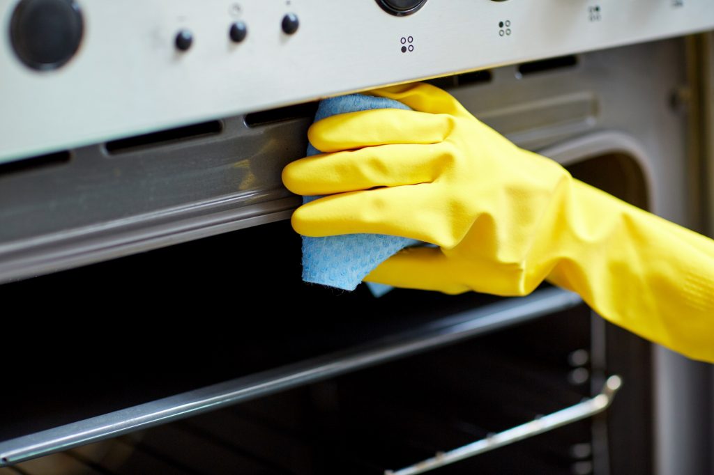 Person's hand in yellow rubber glove cleaning oven with blue cloth
