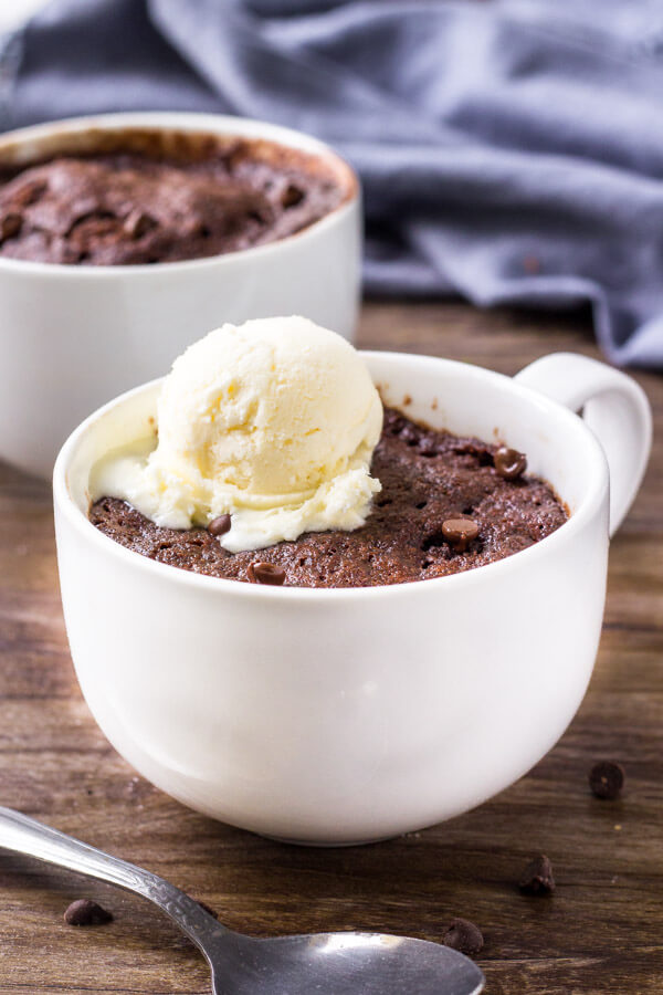 Two white mugs containing chocolate microwave cake, and ice cream on top of front one