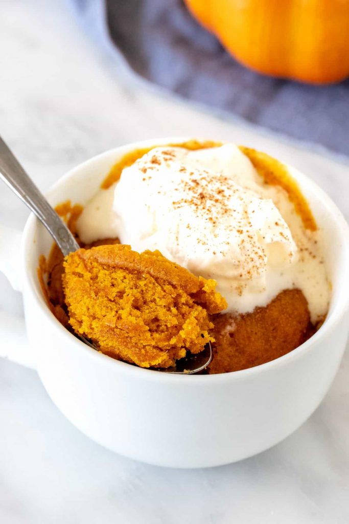 Pumpkin mug cake in white cup with spoon scooping cake out.