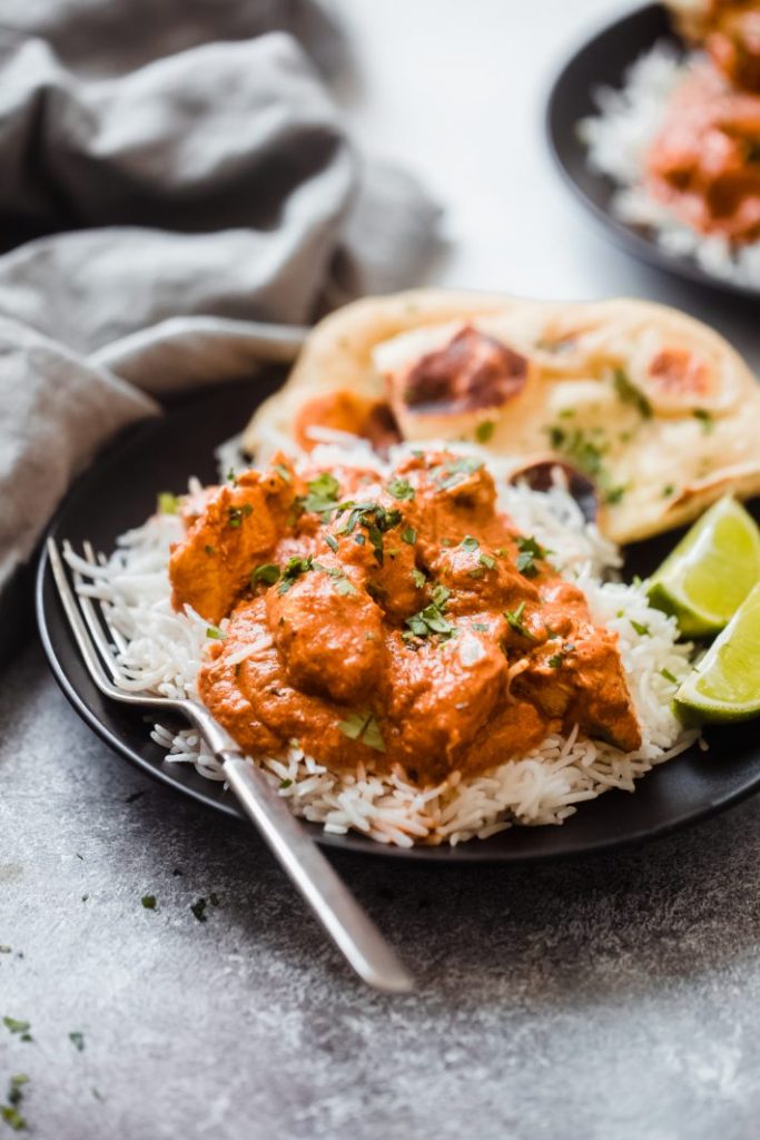 Chicken tikka curry on a bed of rice and served on a black plate with a fork