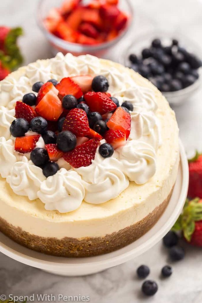 Whole cheesecake decorated with cream swirls, blueberries and sliced fresh strawberries