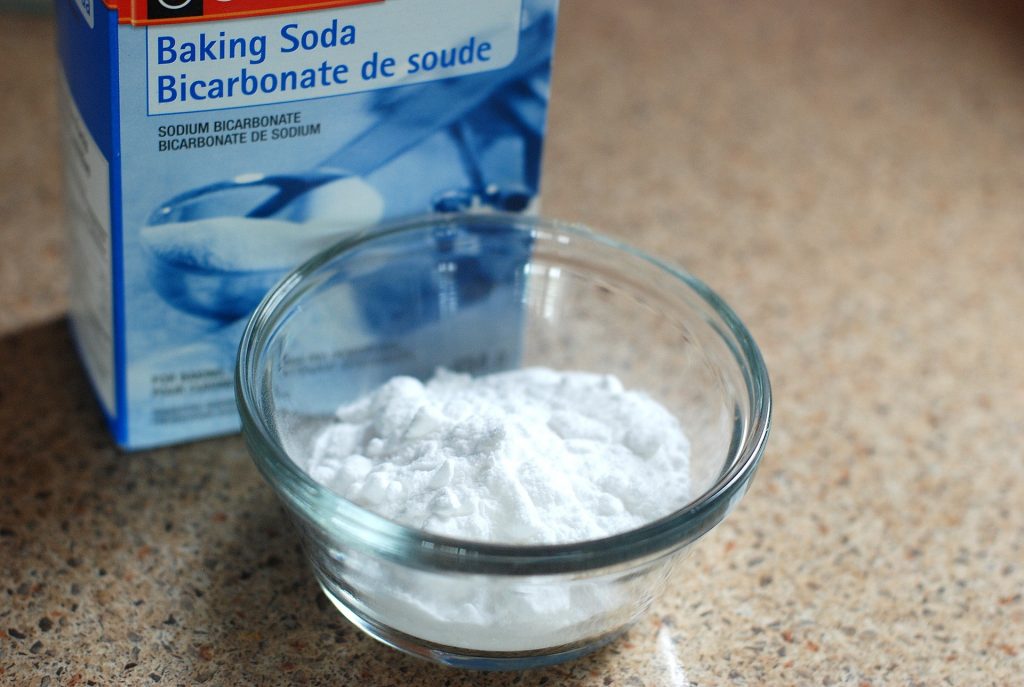 Glass bowl with white powder standing in front of a box labelled baking soda