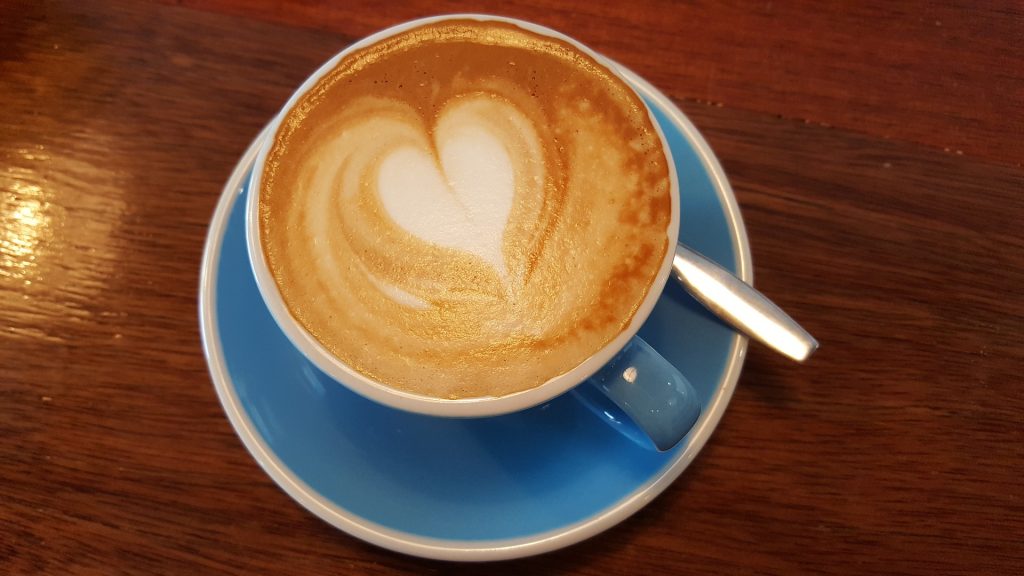 Coffee in a blue cup with a heart shaped design in milk