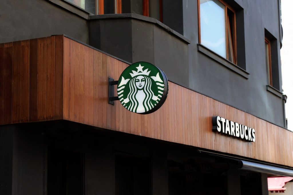 Starbucks store frontage with black building with wooden sign saying Starbucks and another sign with the Starbucks logo