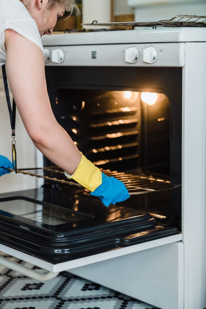 Woman wearing rubber gloves removing rack from oven