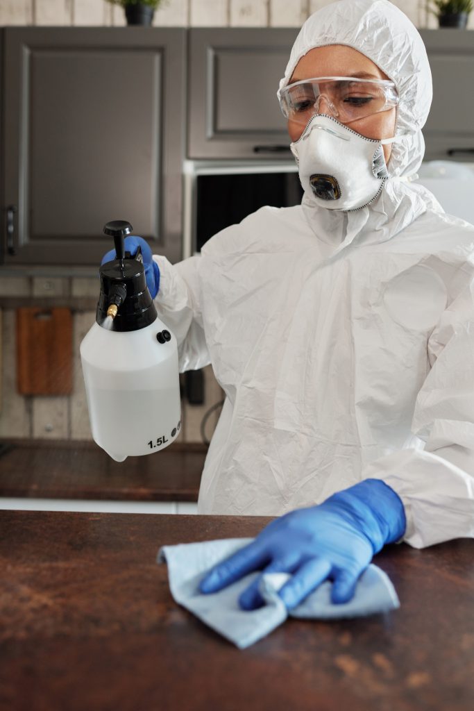 Woman wearing white protective suit and mask spraying cleaning fluid.