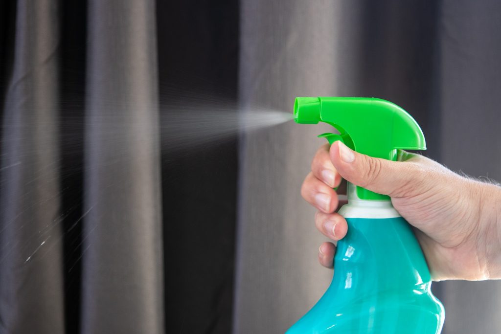 Hand holding a blue and green spray bottle and spraying a clear liquid