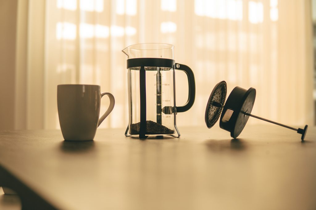 French press with top laying on table with white mug