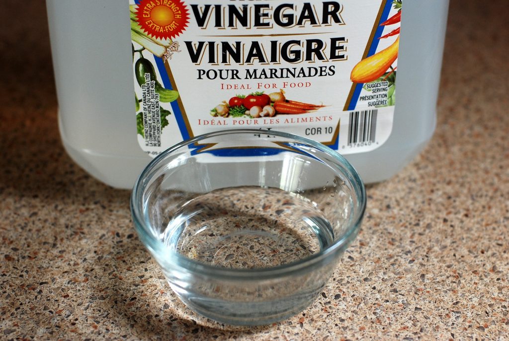 Glass bowl containing clear vinegar in front of container labelled vinegar